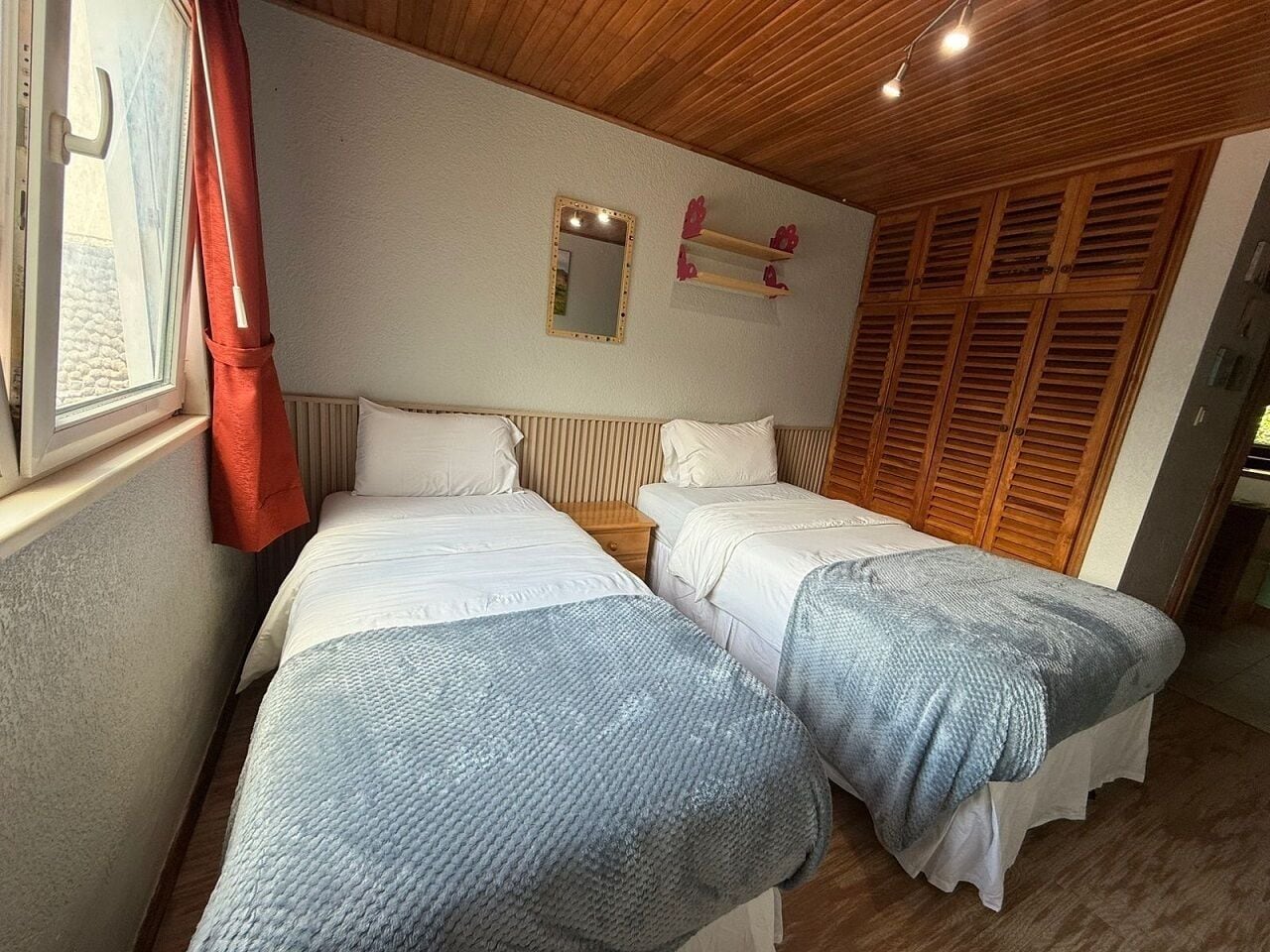 A room with two beds, a window with a curtain, a mirror, and wooden shutters.