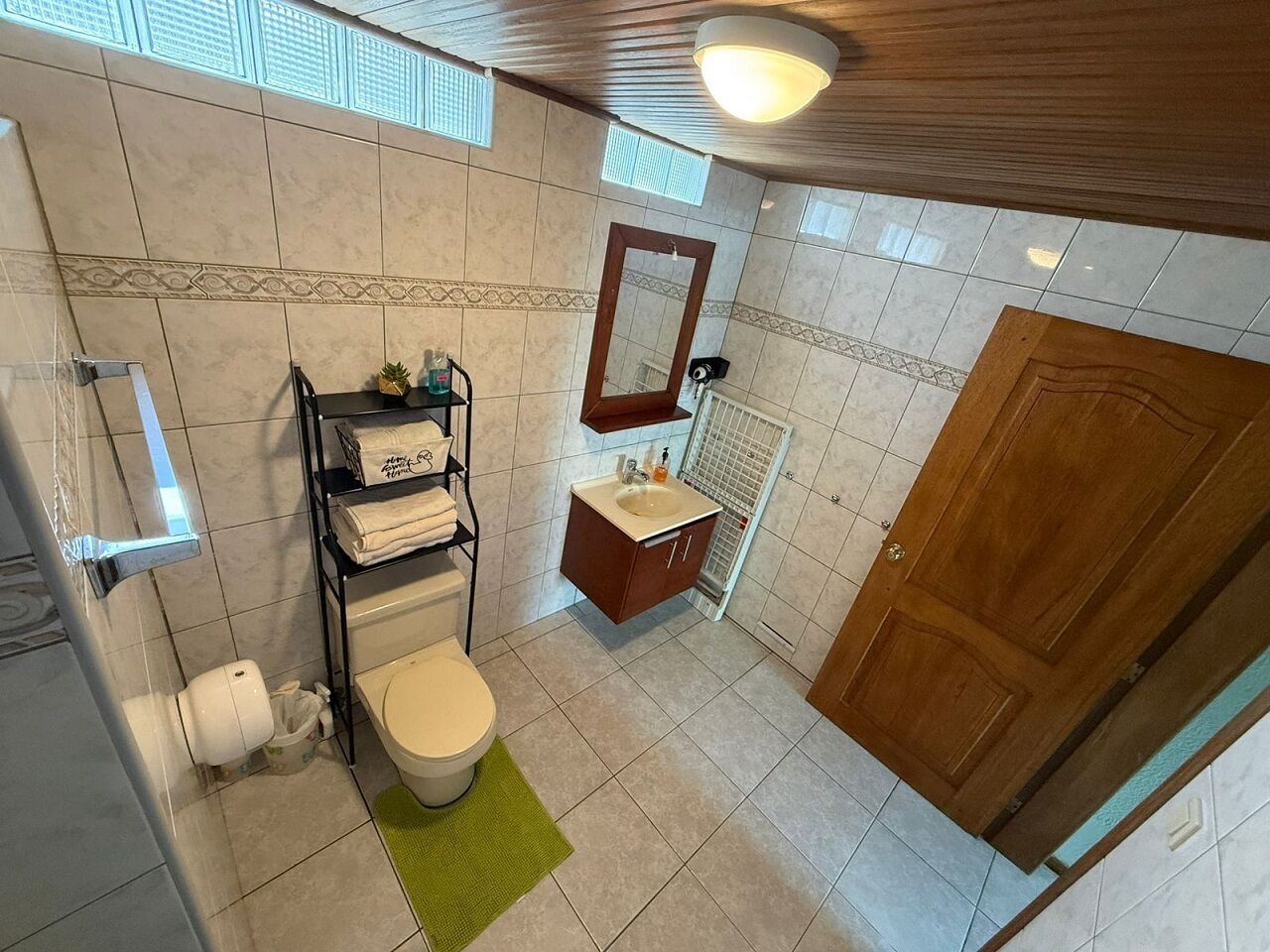 A bathroom with a toilet, sink, mirror, and shelves with toiletries.