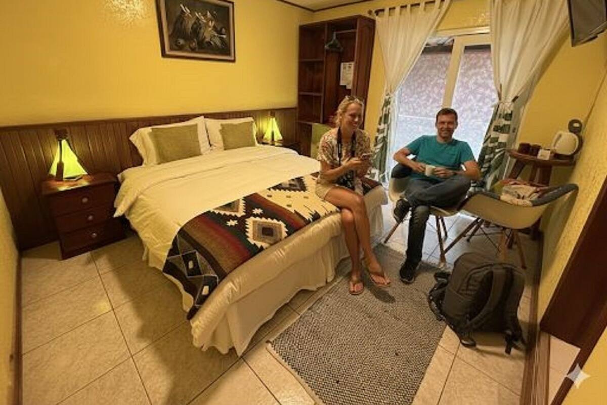 Ein kleines Hotelzimmer mit einem Bett, einem Schreibtisch, einem Stuhl und einem fensterbepflanzten Fenster.
