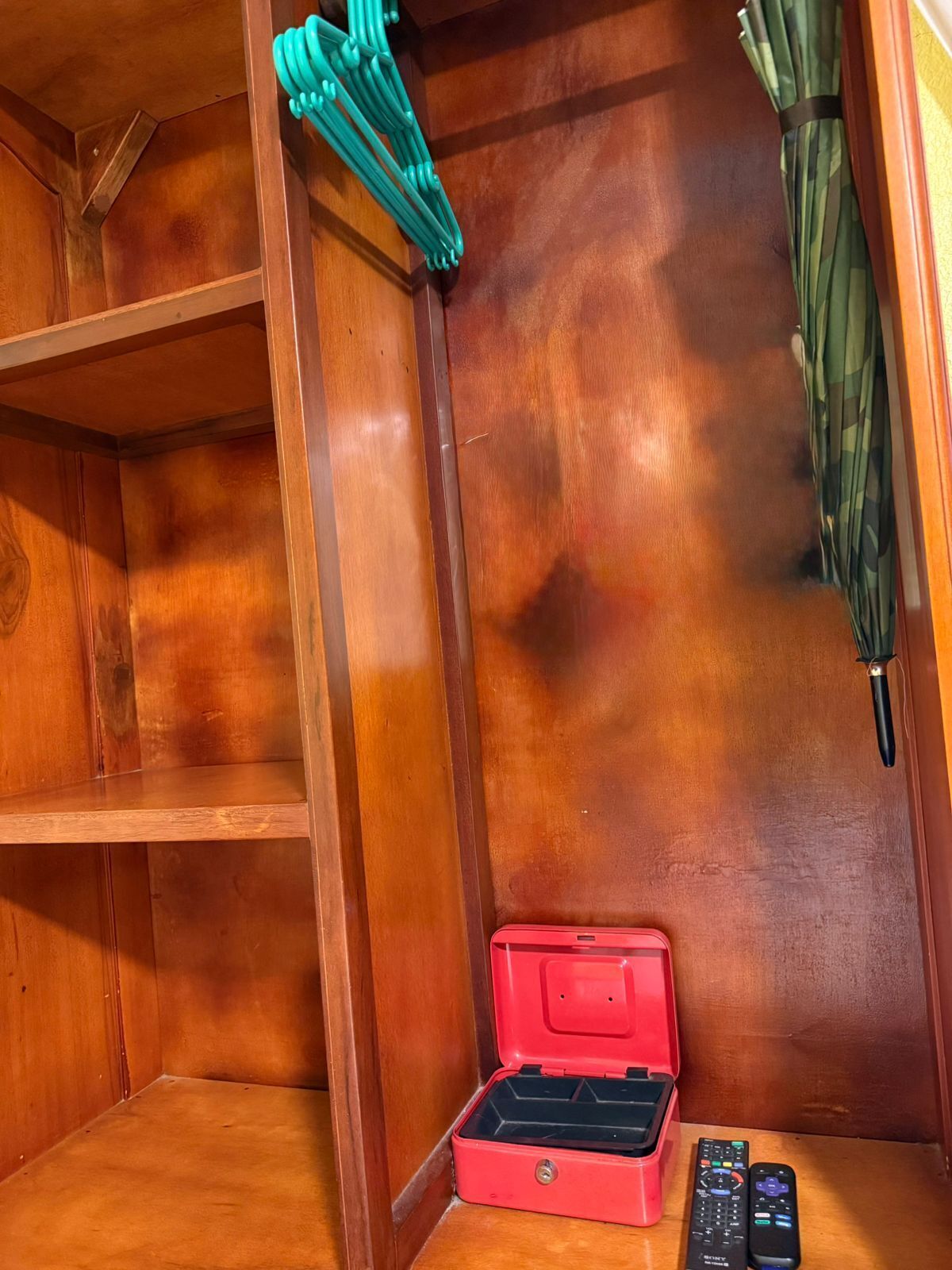 Un armario de madera con una caja roja de almacenamiento y dos mandos a distancia.