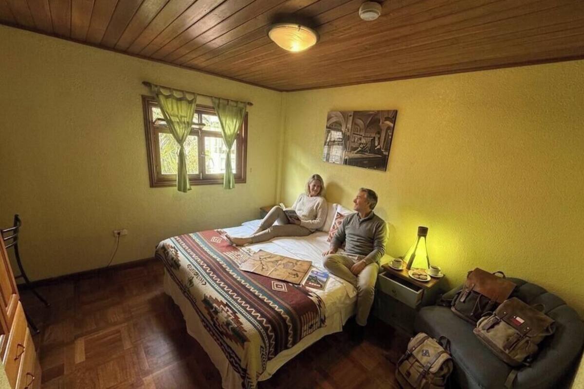 Ein Zimmer mit Bett, Nachttisch, Lampe und einer Couch mit Taschen.