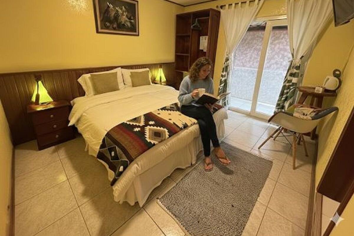 Ein Schlafzimmer mit Bett, Nachttischen, einem Lesesessel und einem Fenster mit Vorhängen.