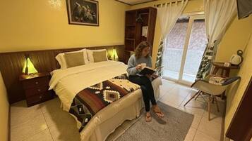 Un dormitorio con cama, mesitas de noche, un sillón de lectura y una ventana con cortinas.