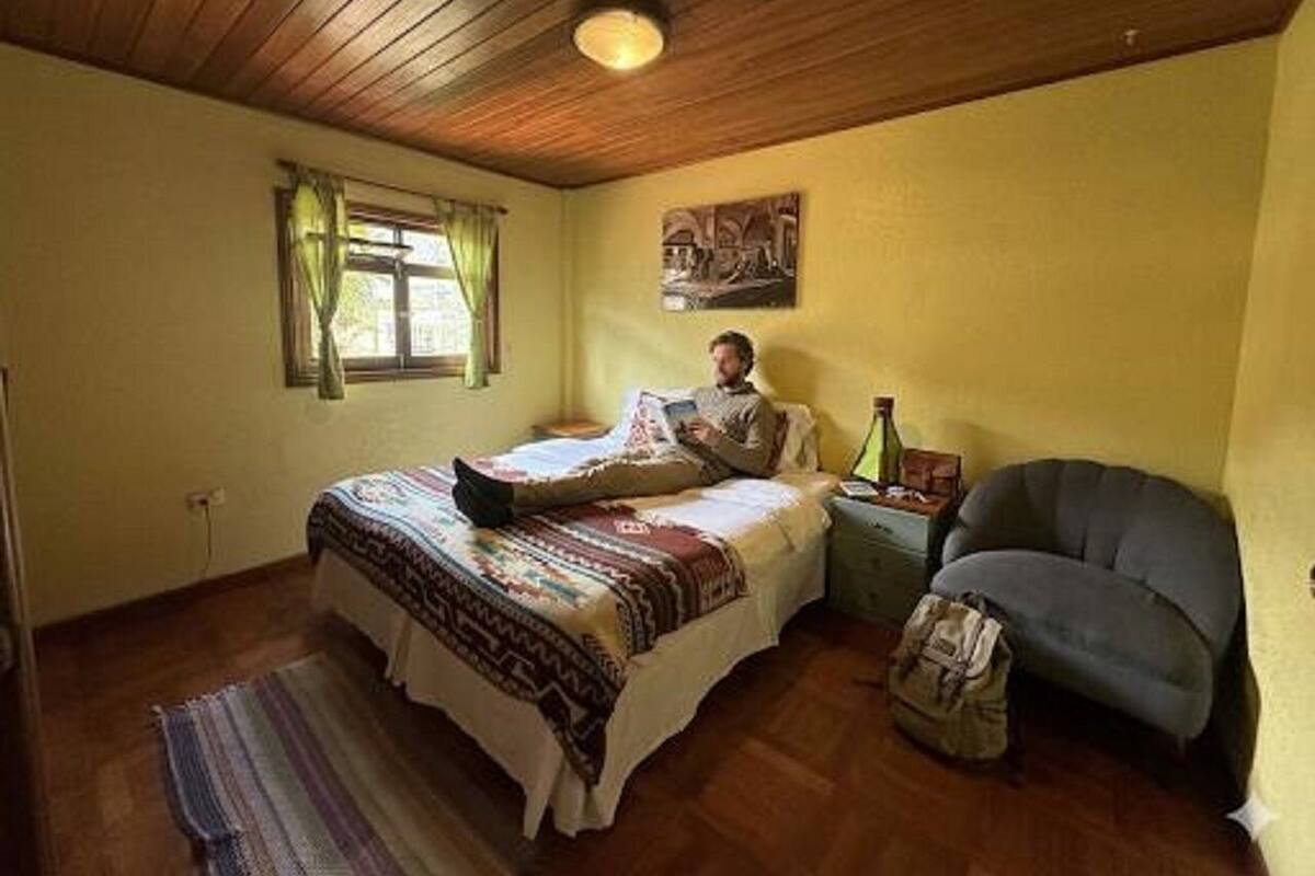 Ein Schlafzimmer mit Bett, einem Fenster mit Vorhängen, einem Bild an der Wand und einem Sessel.