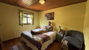 Un dormitorio con una cama, una ventana con cortinas, un cuadro en la pared y una silla.