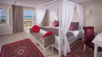Een slaapkamer met een hemelbed, een bankje en een stoel, met uitzicht op een balkon.