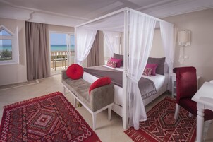A bedroom with a four-poster bed, a bench, and a chair, with a balcony view.