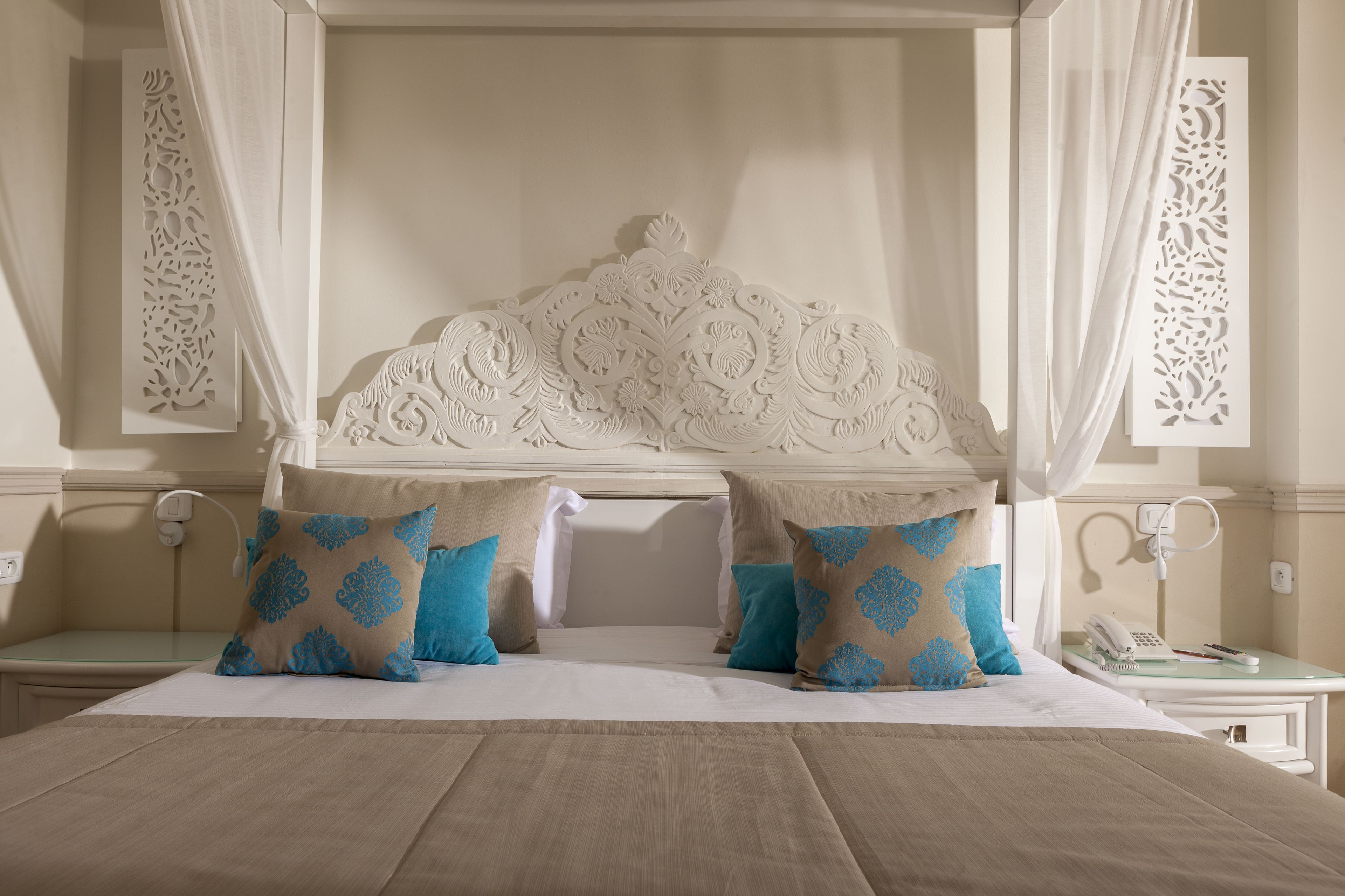 Una cama con dosel, una mesita de noche con teléfono y una pared con paneles decorativos.