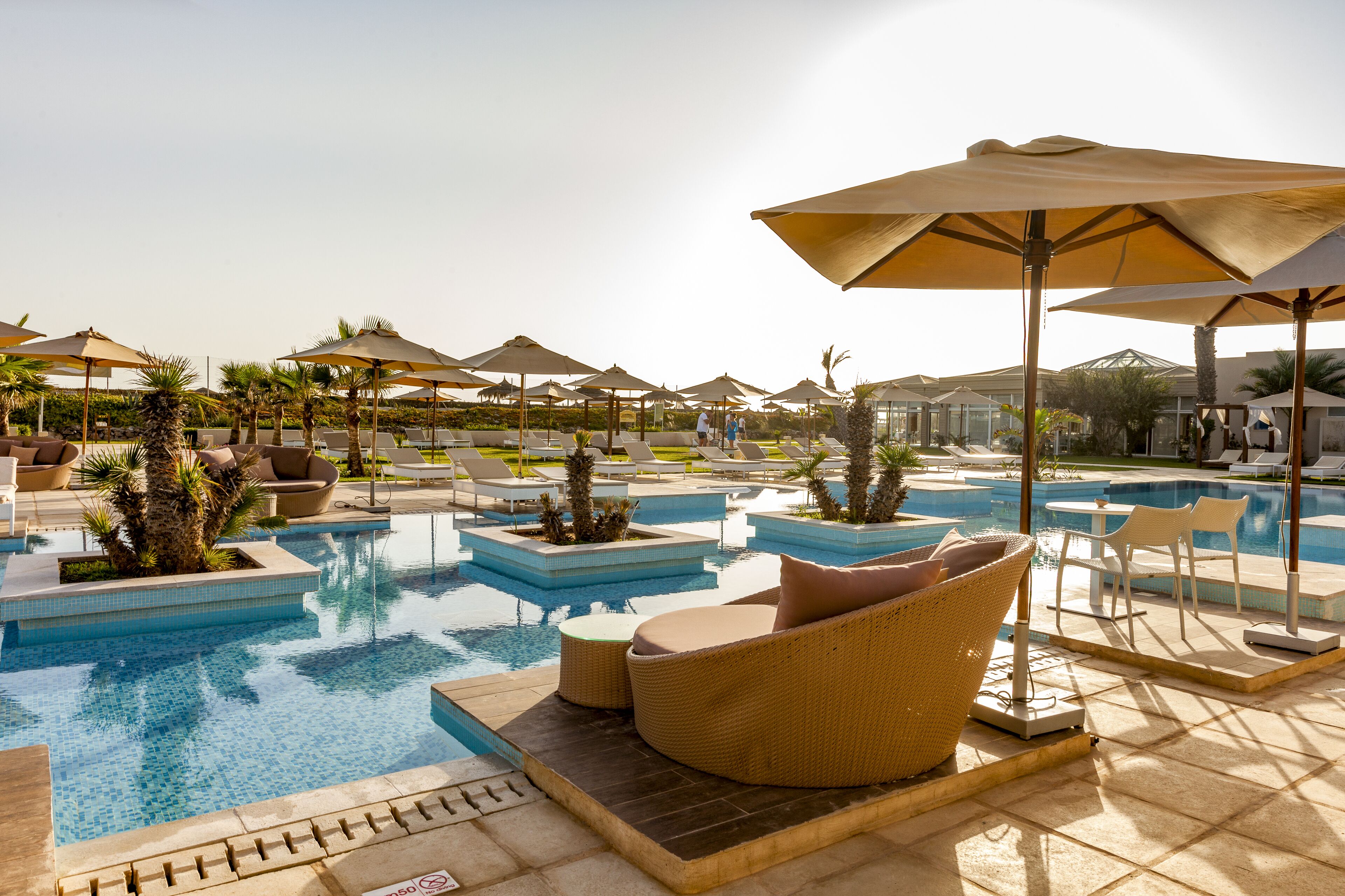 Un espace aménagé au bord de la piscine, avec des chaises longues, des parasols et une vue dégagée sur la piscine.