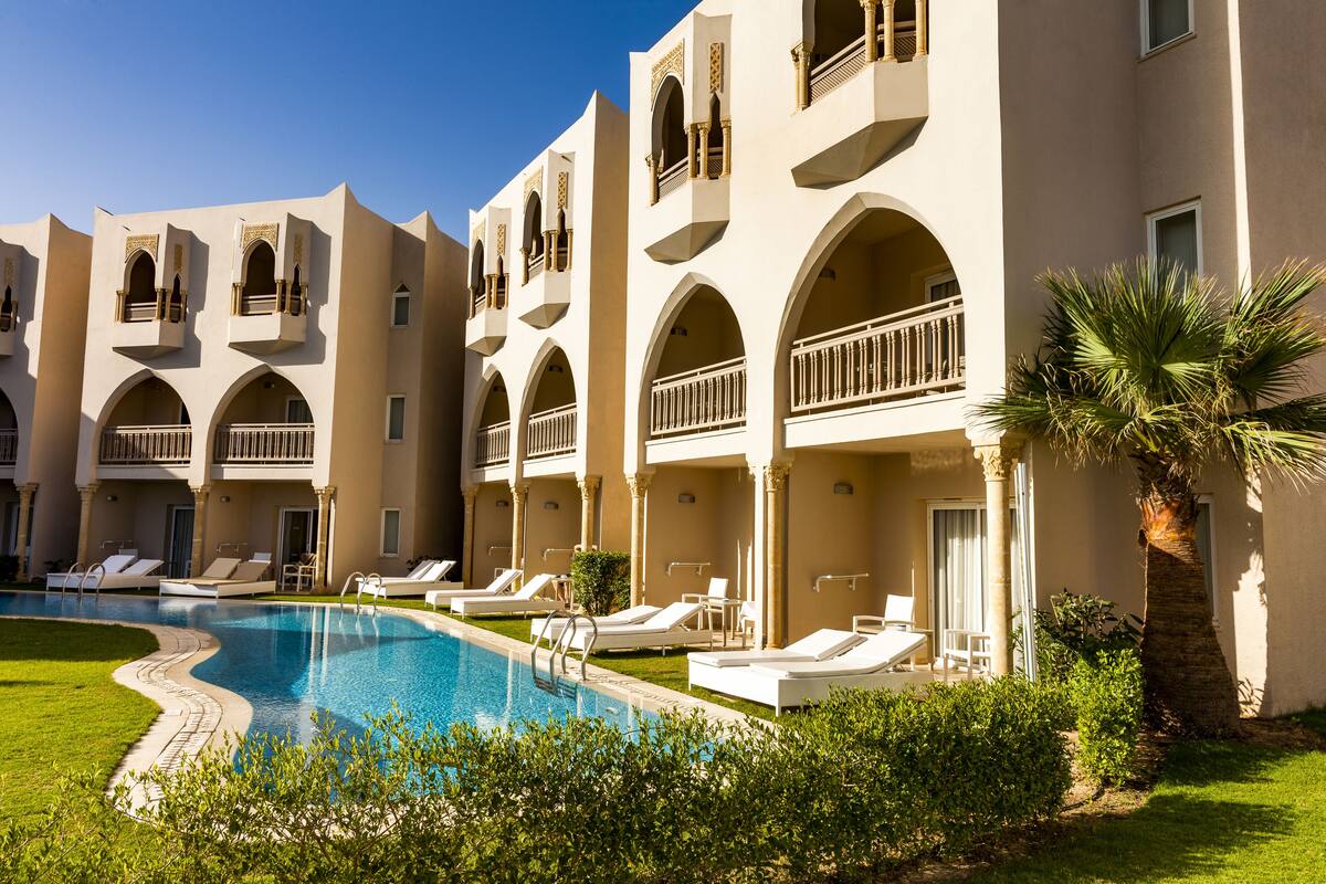 A hotel with multiple balconies, a swimming pool, and sun loungers.