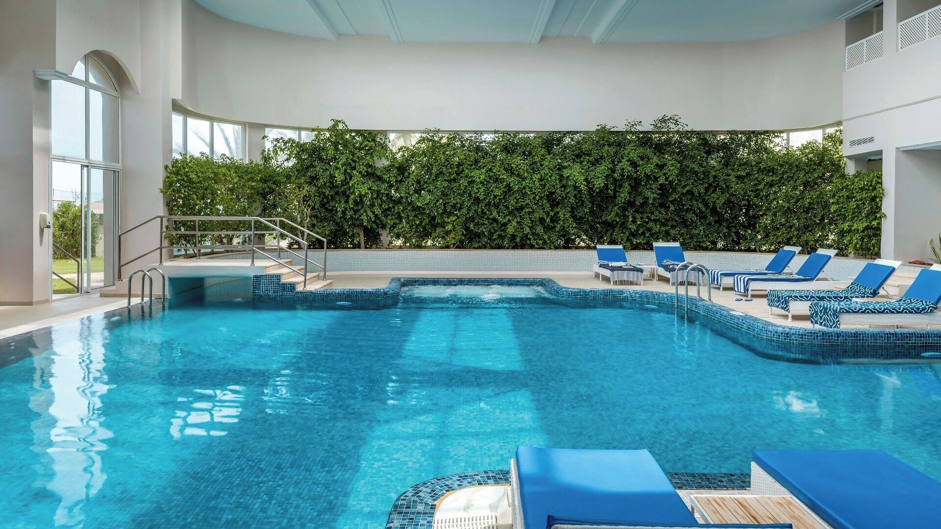 Une piscine à l’eau d’un bleu cristallin, entourée de chaises longues et d’un escalier menant à un niveau supérieur.