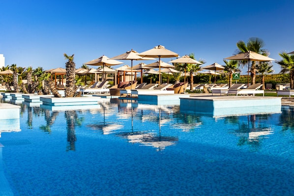 Una piscina al aire libre, sombrillas, sillones reclinables de piscina