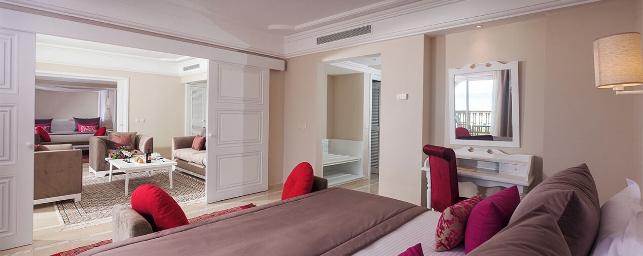 A spacious bedroom with a large bed, a sitting area with a sofa and coffee table, and a walk-in closet.