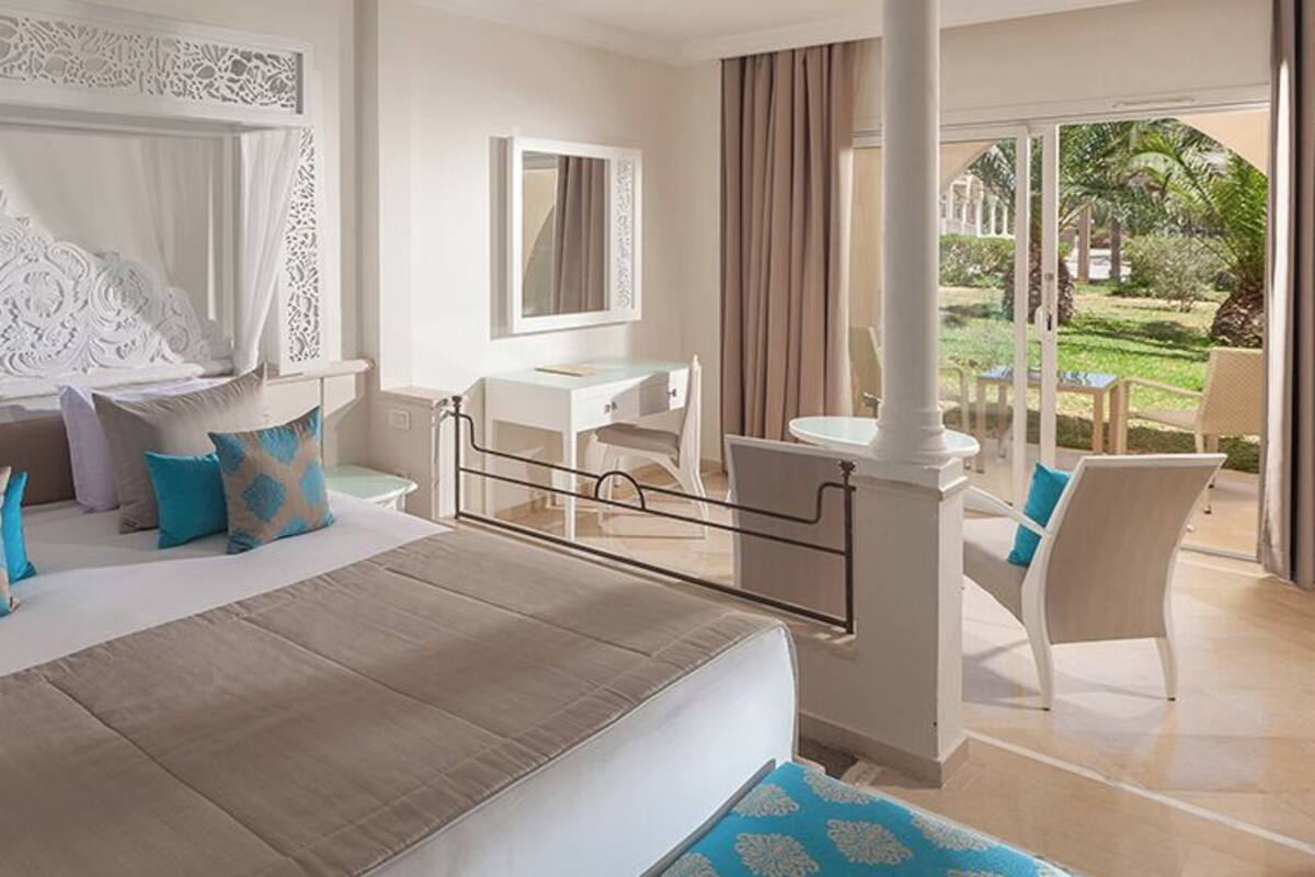 A hotel room with a large bed, a desk, and a view of the garden.