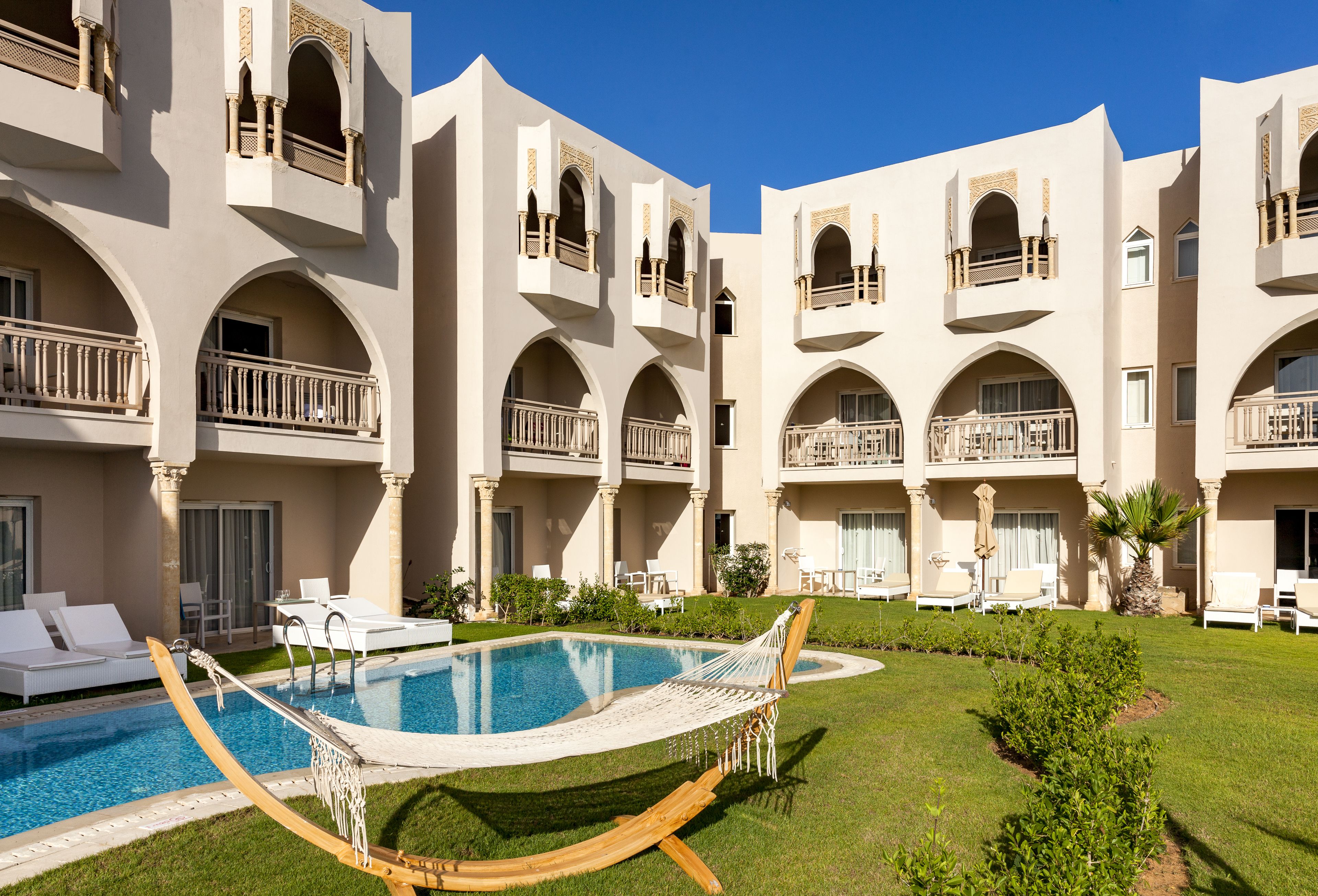 Un patio de hotel con piscina, mobiliario exterior y varios balcones.