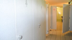 Une rangée de toilettes publiques blanches, avec un sol carrelé et une poignée de porte visible sur la première porte, à gauche.