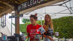 Une installation temporaire en plein air pour un événement, comprenant une tente, un comptoir avec une pancarte indiquant « THE LEGAL », ainsi que divers conteneurs et objets disposés au sol.