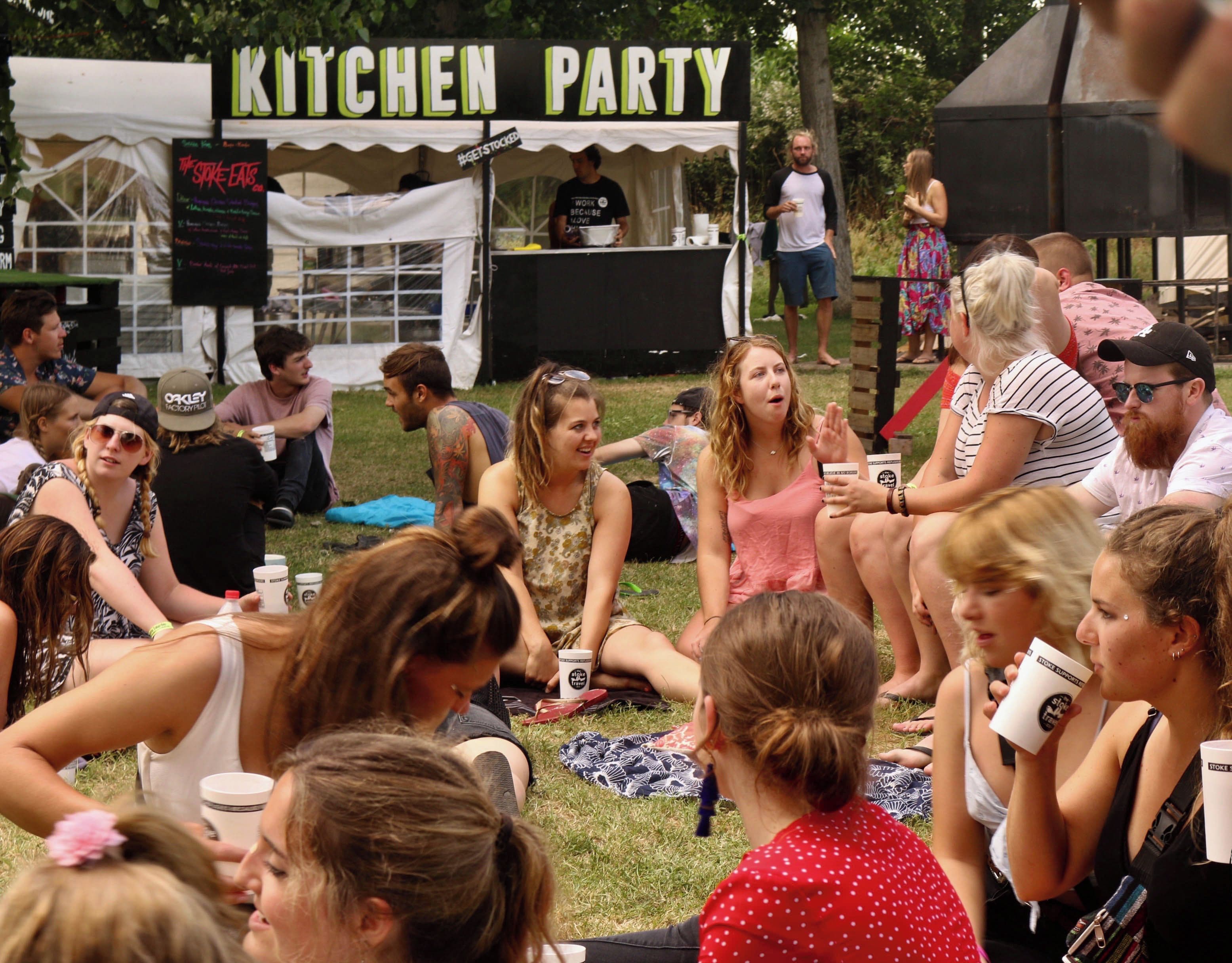 Un groupe de personnes s’est rassemblé autour d’une tente sur laquelle était écrit « Kitchen Party », et un panneau indiquait « Stoke Travel Co. ».