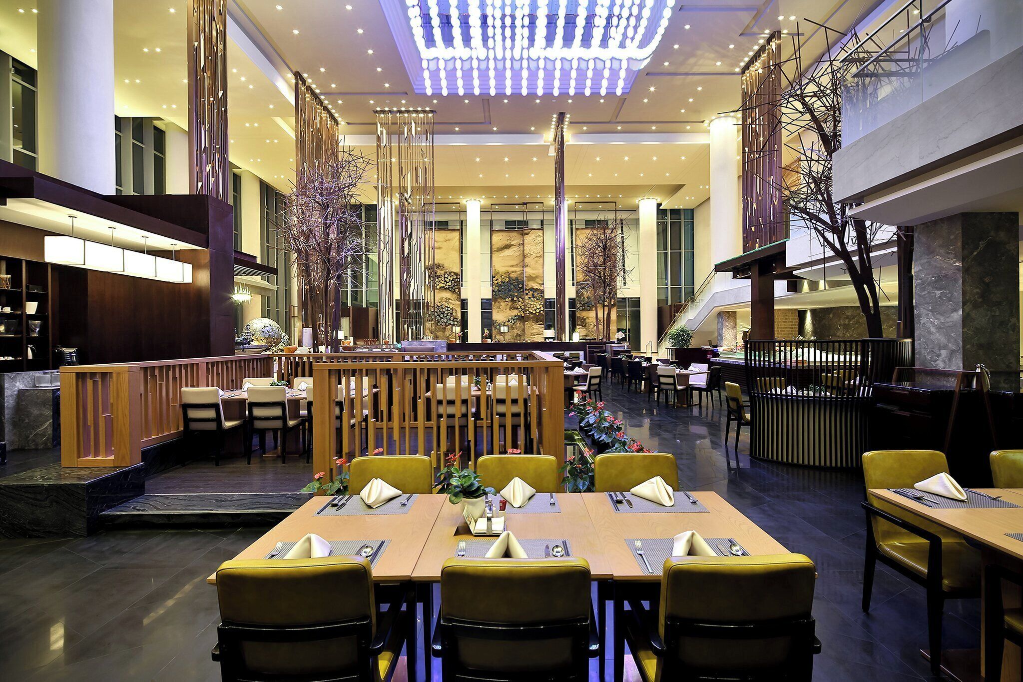 A spacious restaurant with high ceilings, modern lighting, and a central seating area with tables and chairs.