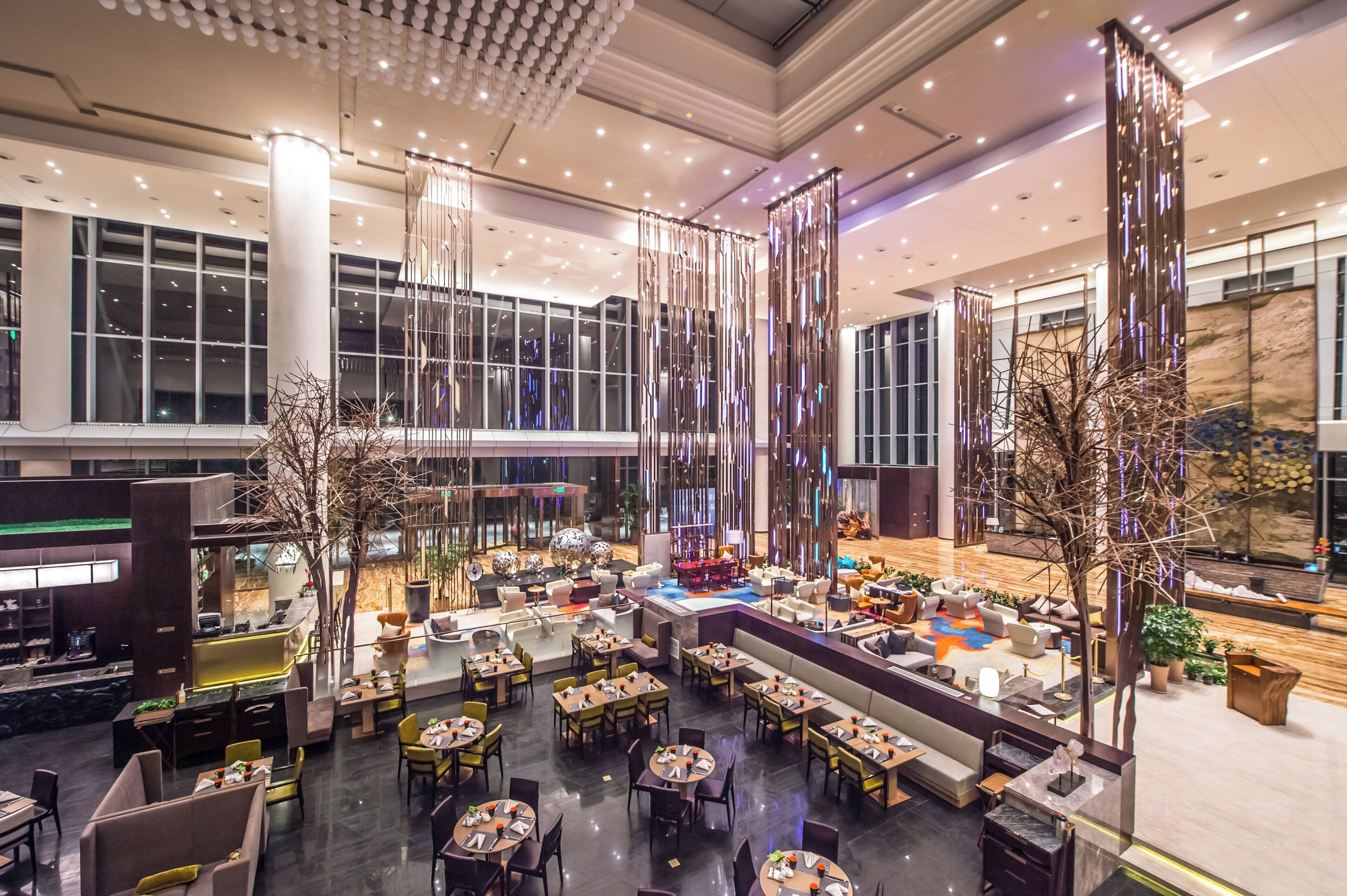 A spacious hotel lobby with multiple seating areas, including a bar and dining tables.