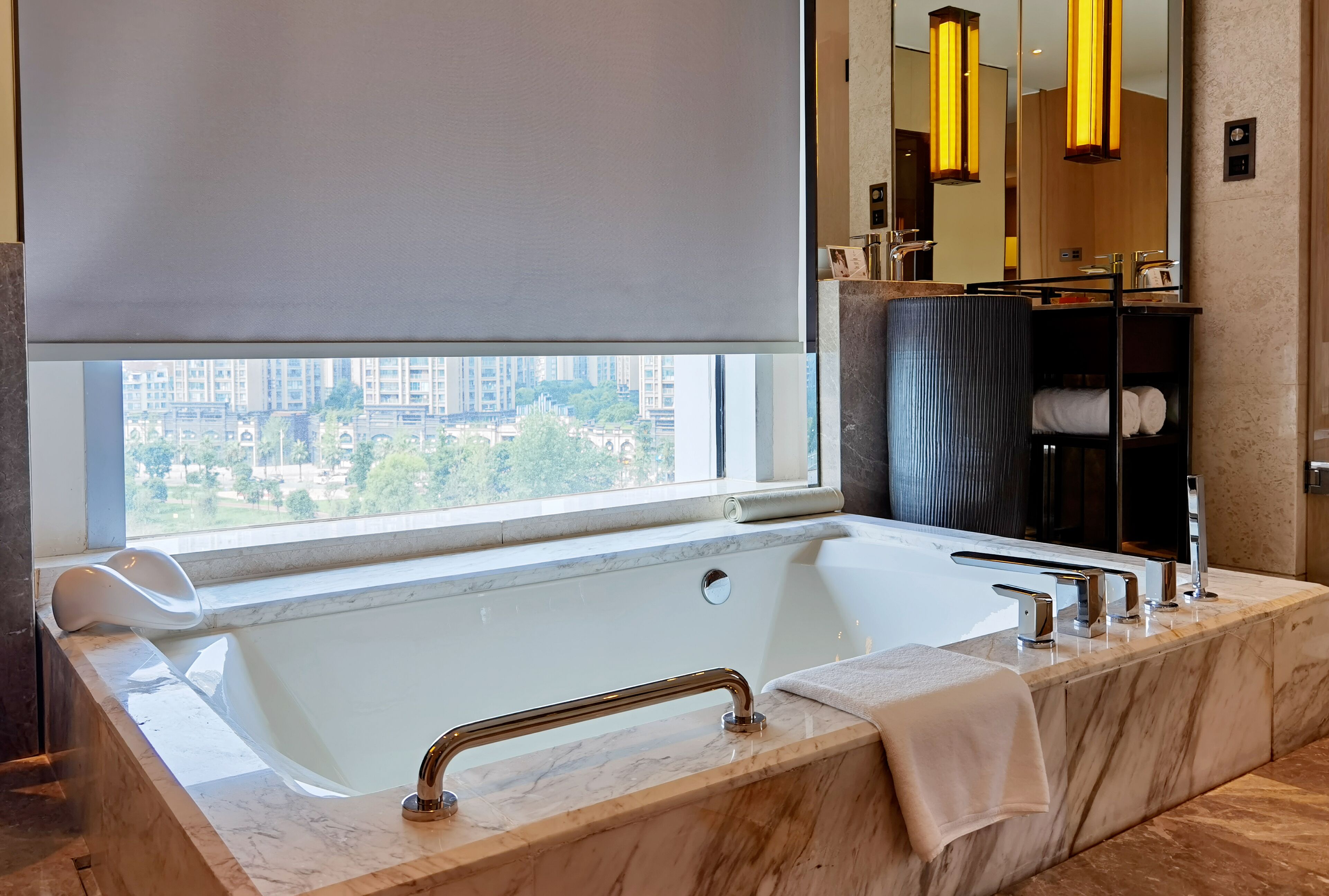 A modern bathroom with a large bathtub, a vanity with a mirror, and a view of the city through a large window.