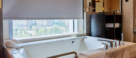 A modern bathroom with a large bathtub, a vanity with a mirror, and a view of the city through a large window.