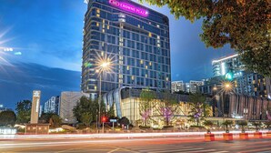 A modern high-rise hotel with a prominent "Crowne Plaza" sign, surrounded by urban infrastructure and nighttime lighting.