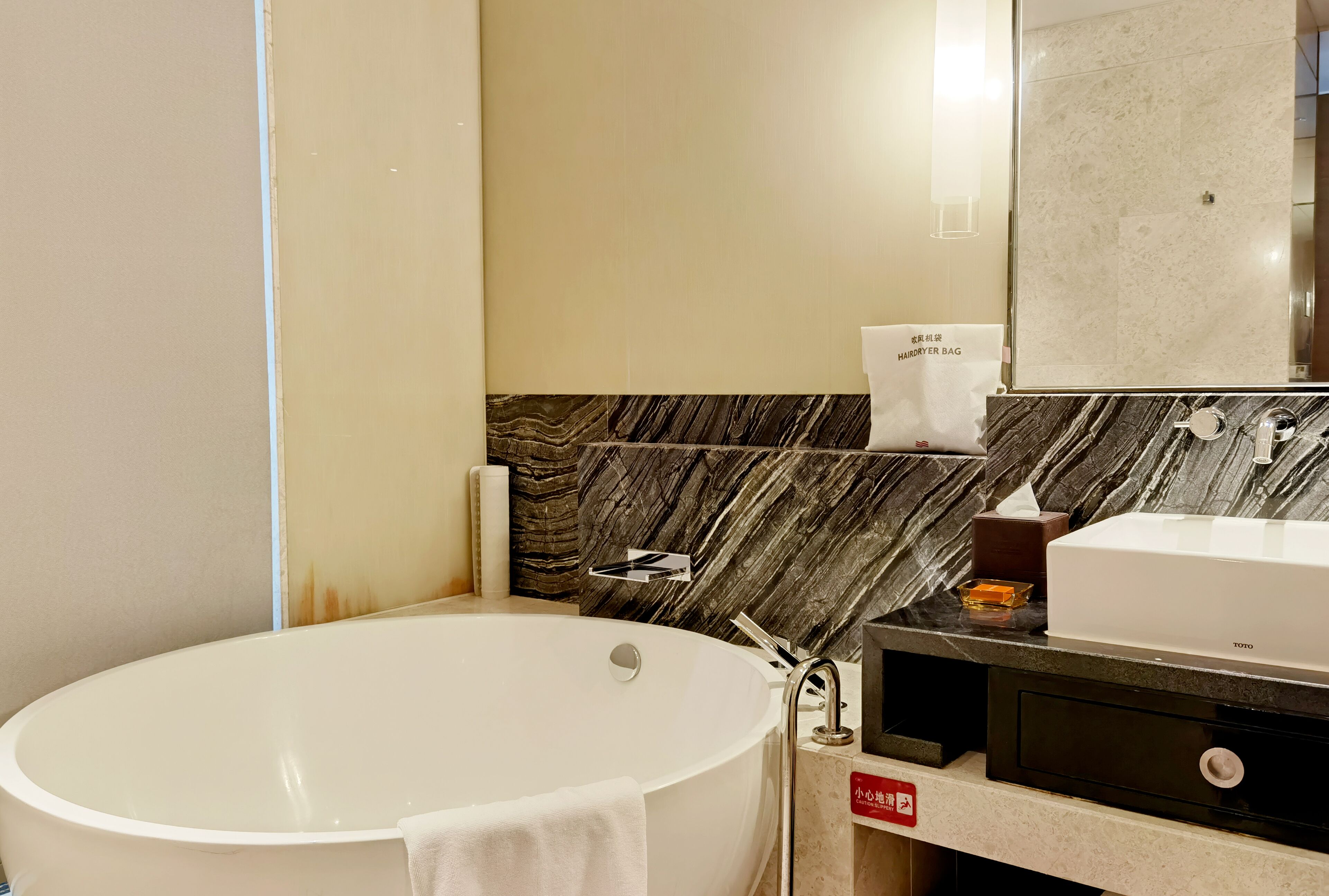 A modern bathroom with a freestanding bathtub, a vanity with a mirror, and a marble backsplash.