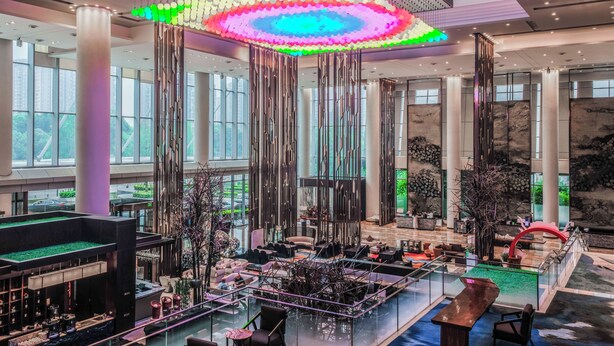 A spacious lobby with a high ceiling, large windows, and a central seating area with a glass barrier.