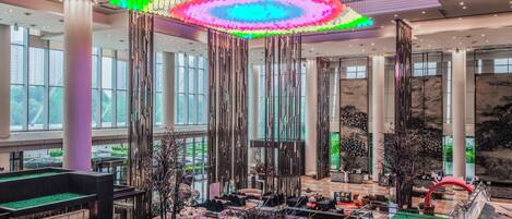 A spacious lobby with a high ceiling, large windows, and a central seating area with a glass barrier.