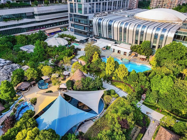 Ein moderner Hotelkomplex mit Schwimmbad, üppiger Bepflanzung und zeitgenössischer Architektur.