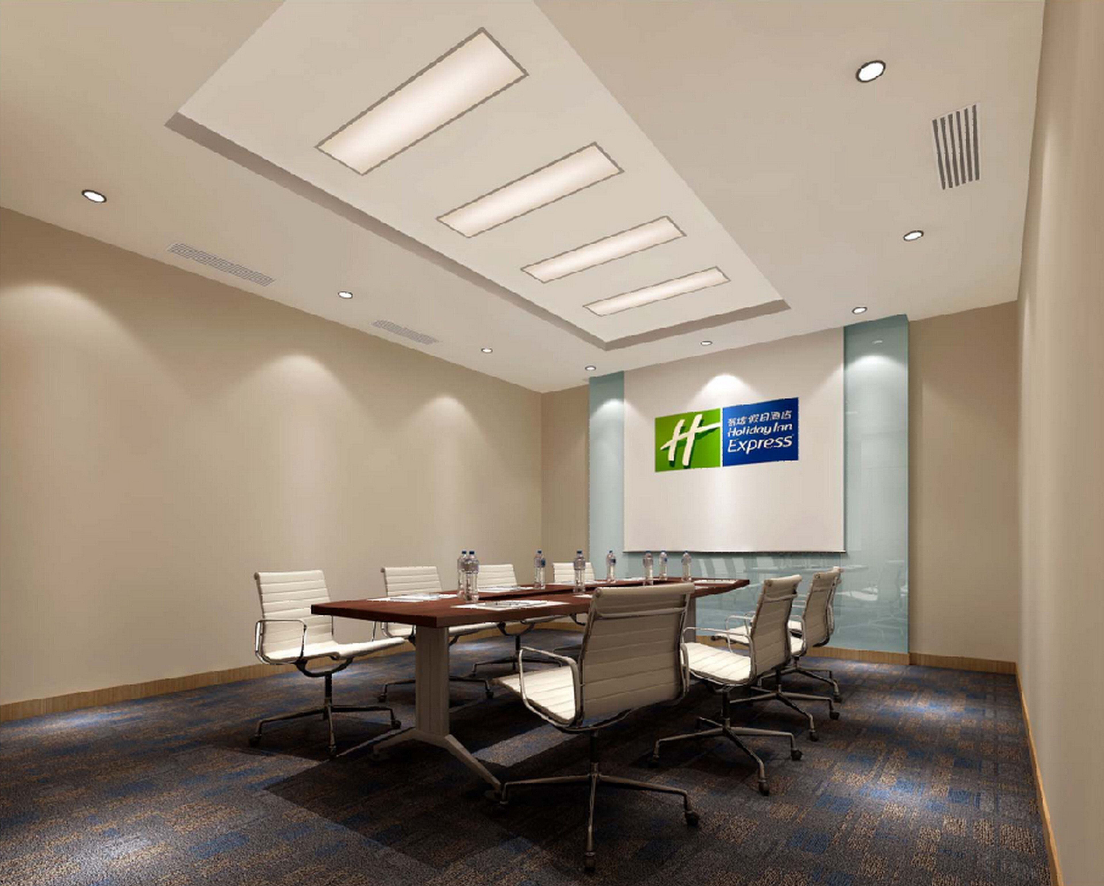 A conference room with a long table, six chairs, and a large screen displaying a logo.