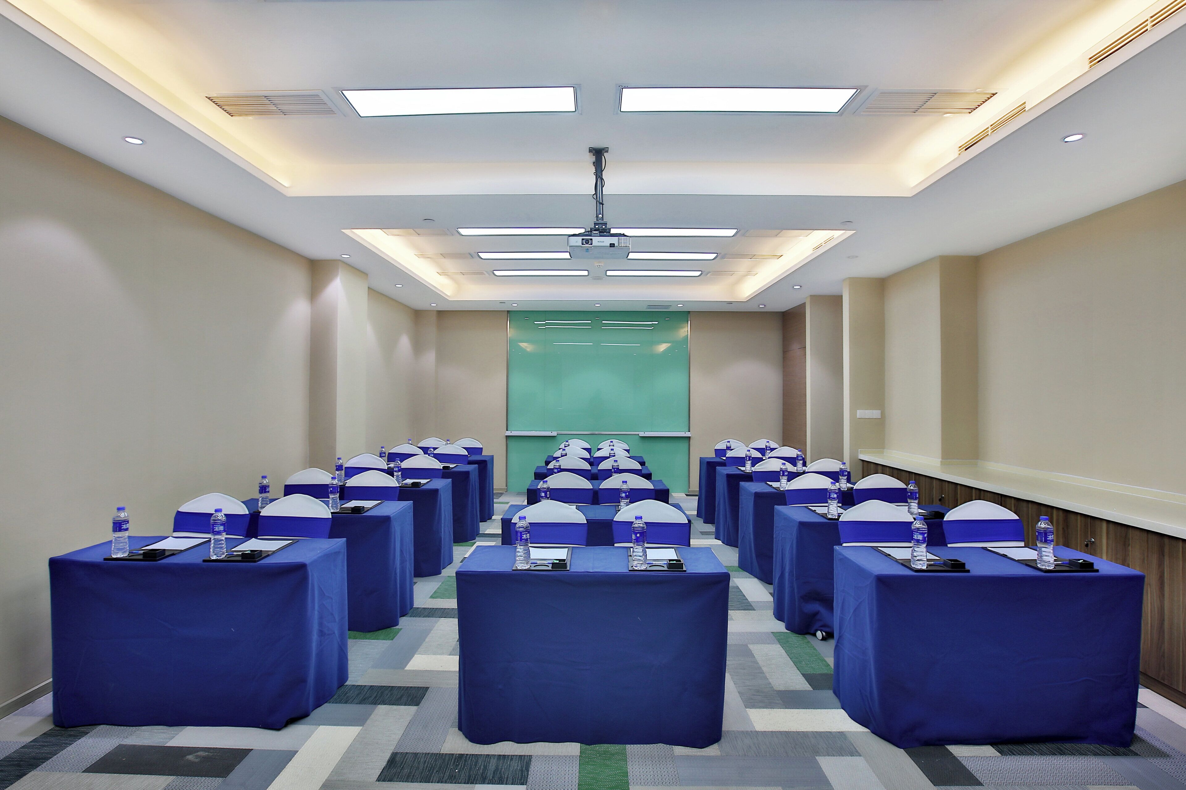 Un salón de conferencias con filas de mesas, cada una con una botella de agua y un bloc de notas.