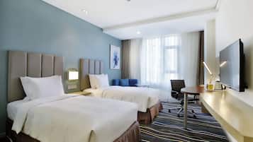 Habitación de hotel con dos camas, un escritorio, una silla, un televisor y una ventana con cortinas.
