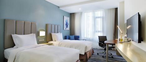 A hotel room with two beds, a desk, a chair, a television, and a window with curtains.