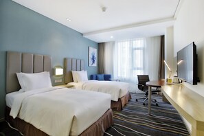 Ein Hotelzimmer mit zwei Betten, einem Schreibtisch, einem Stuhl, einem Fernseher und einem Fenster mit Vorhängen.