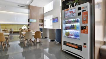 Un moderno vestíbulo de hotel con una máquina expendedora, zona de estar y una televisión.