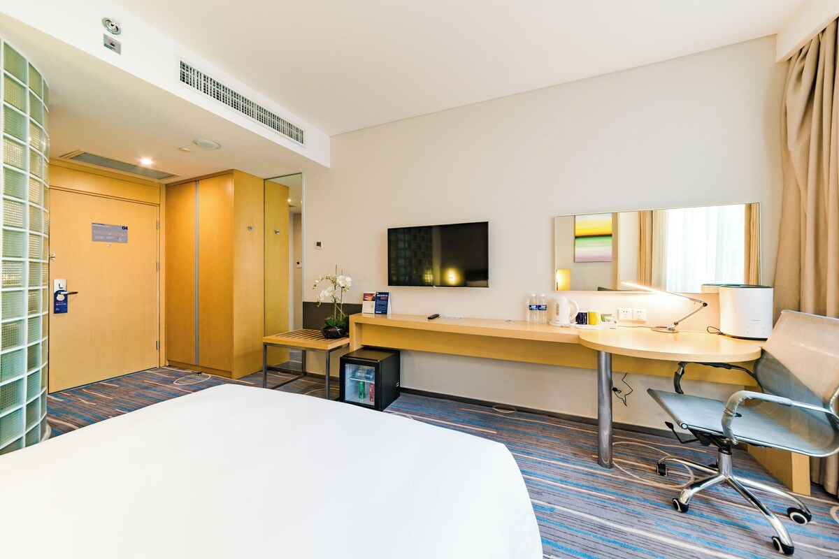 Ein Hotelzimmer mit Bett, Schreibtisch, Stuhl, Fernseher und kleinem Kühlschrank.