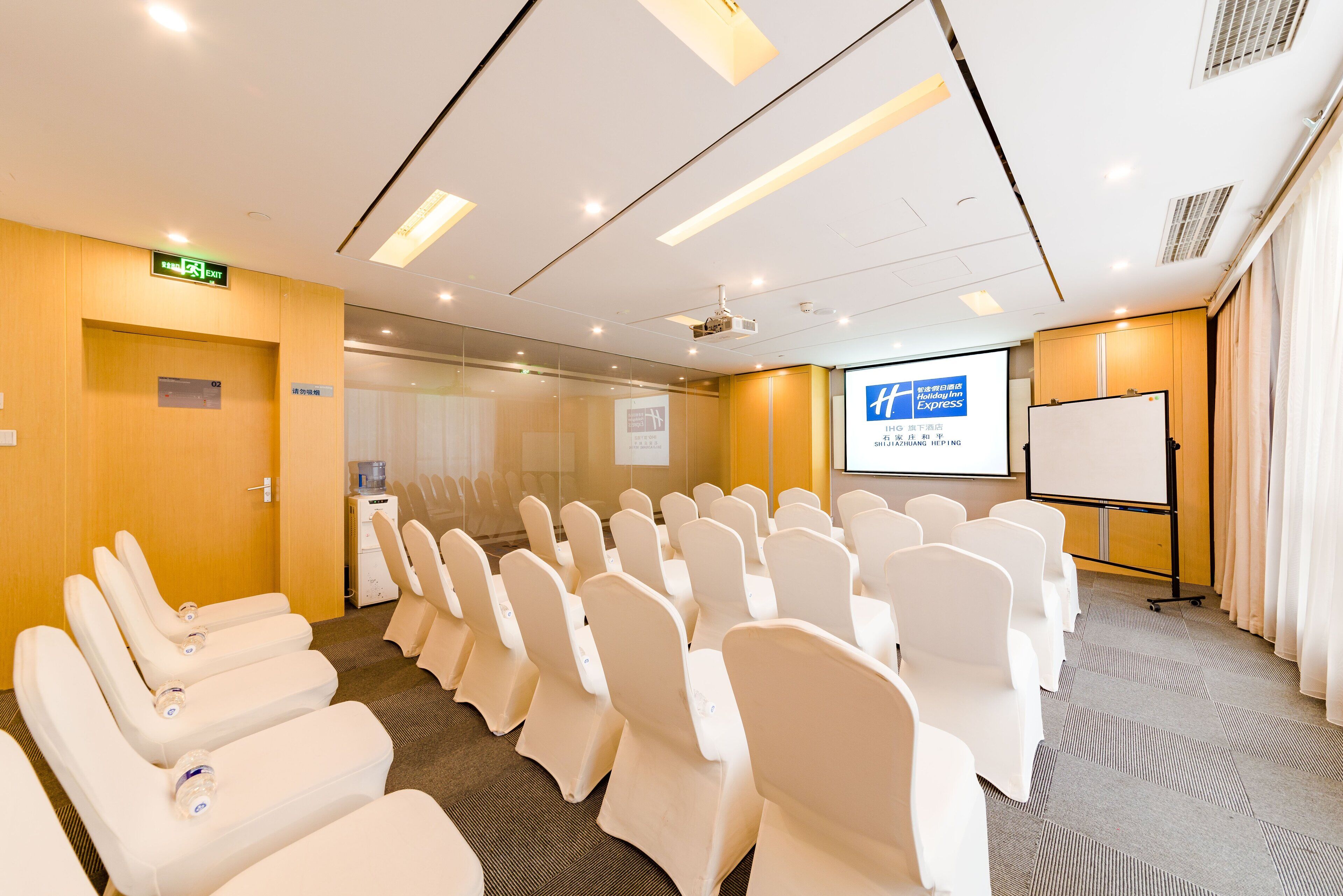 A conference room with rows of white chairs, a projector screen, and a whiteboard.
