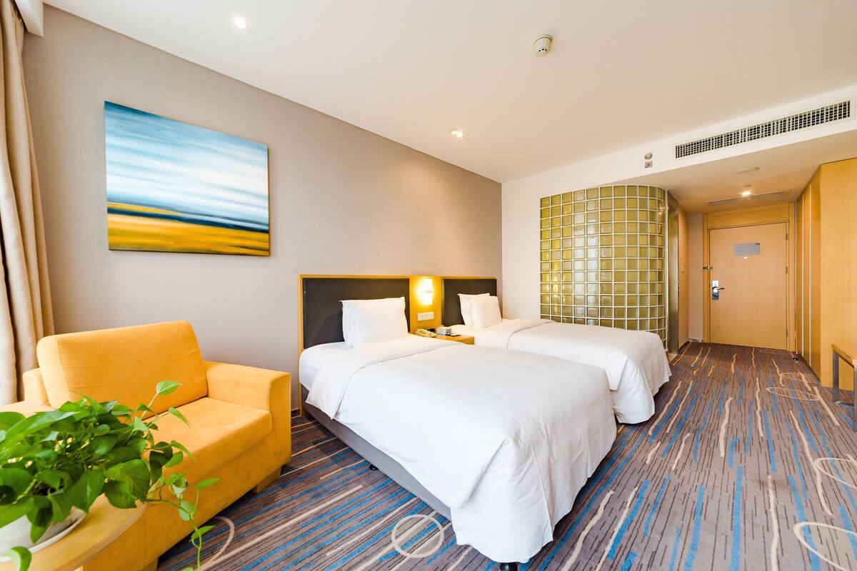 Une chambre d’hôtel avec deux lits, un canapé, un tableau et une grande fenêtre.