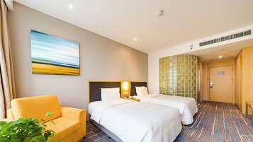 A hotel room with two beds, a sofa, a painting, and a plant.