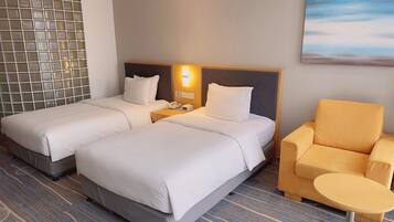 Een hotelkamer met twee bedden, een nachtkastje met telefoon en lamp, een klein rond tafeltje en een stoel.