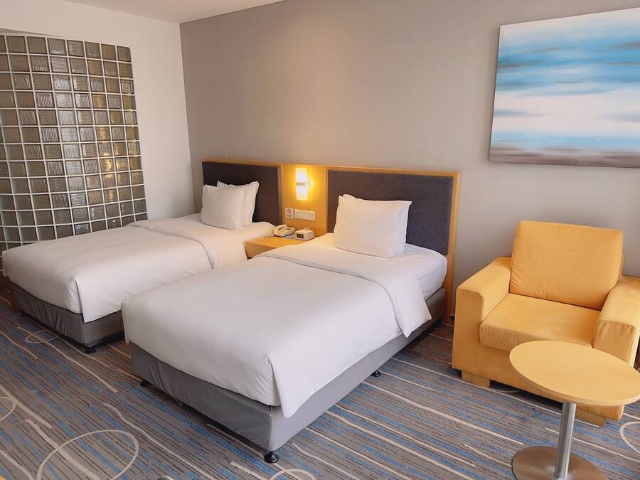 Een hotelkamer met twee bedden, een nachtkastje met telefoon en lamp, een klein rond tafeltje en een stoel.