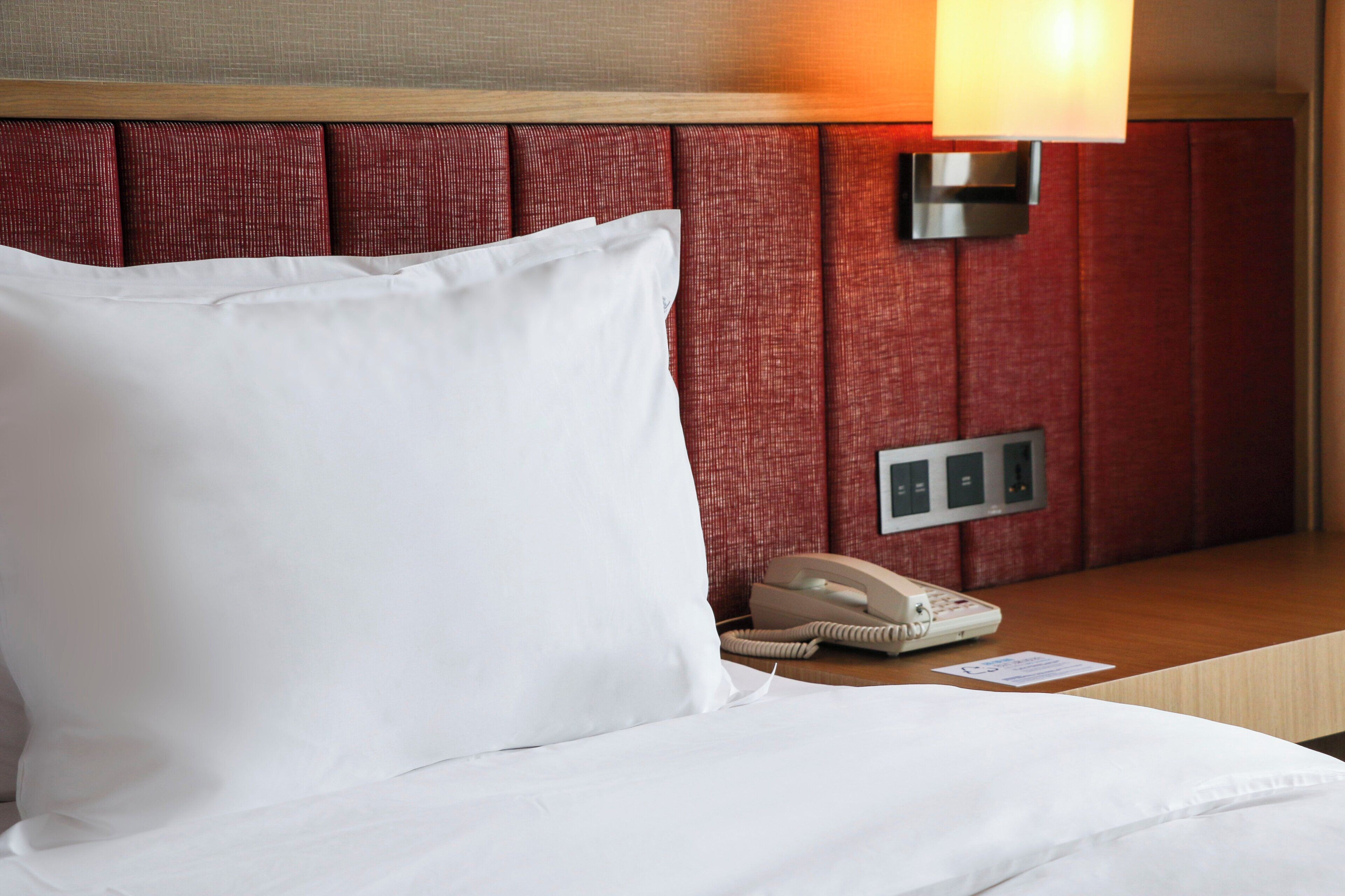 Een hotelkamer met een bed, een bedlamp, een telefoon en een paneel met een schakelaar.