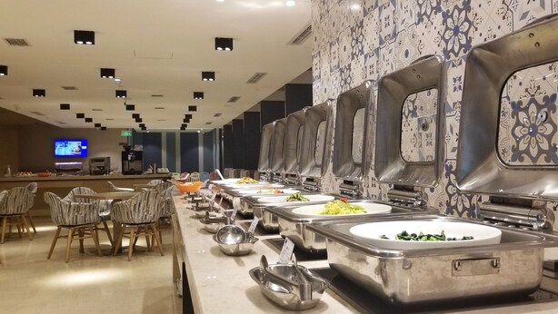 A buffet setup with multiple serving stations, a counter with a television, and patterned wall tiles. - Holiday Inn Express Chengdu Wenjiang Hotspring by IHG (Chengdu)