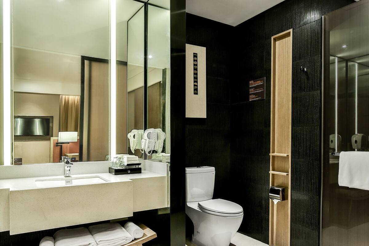 A modern bathroom with a large mirror, a sink, a toilet, and a towel rack.