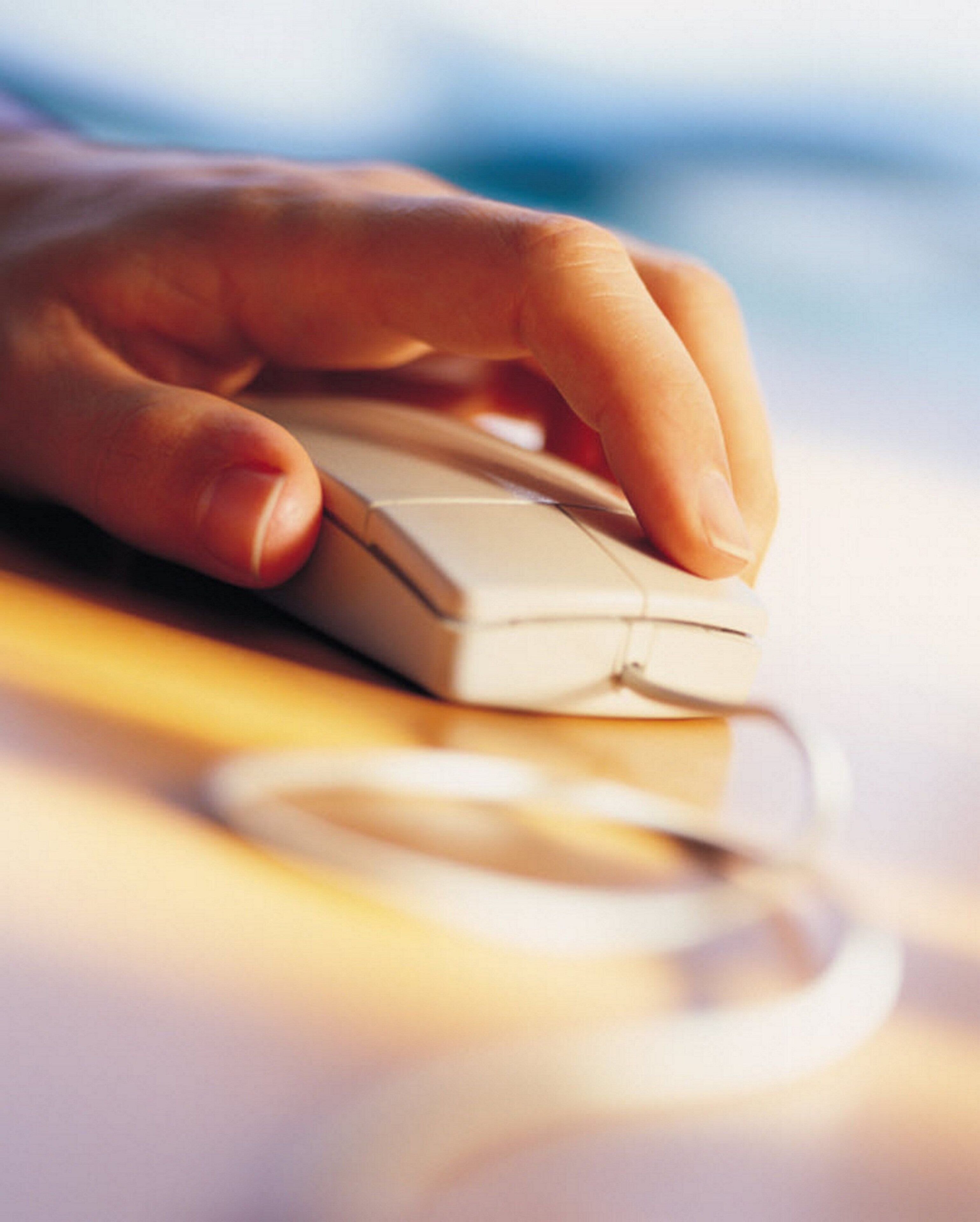 Mão usando um rato de computador branco sobre uma superfície plana.