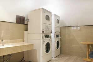 Een wasserette met gestapelde wasmachines, een wasbak en een klein houten tafeltje.