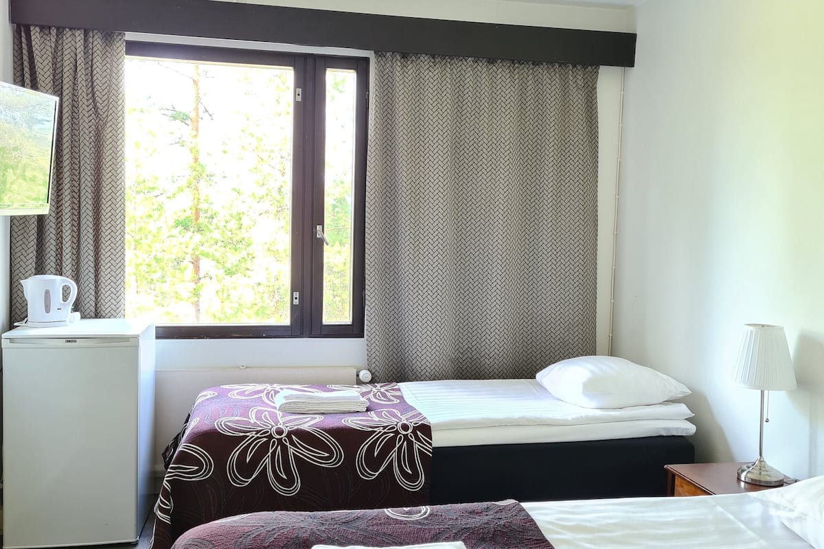A hotel room with two beds, a desk, a kettle, and a window with curtains.