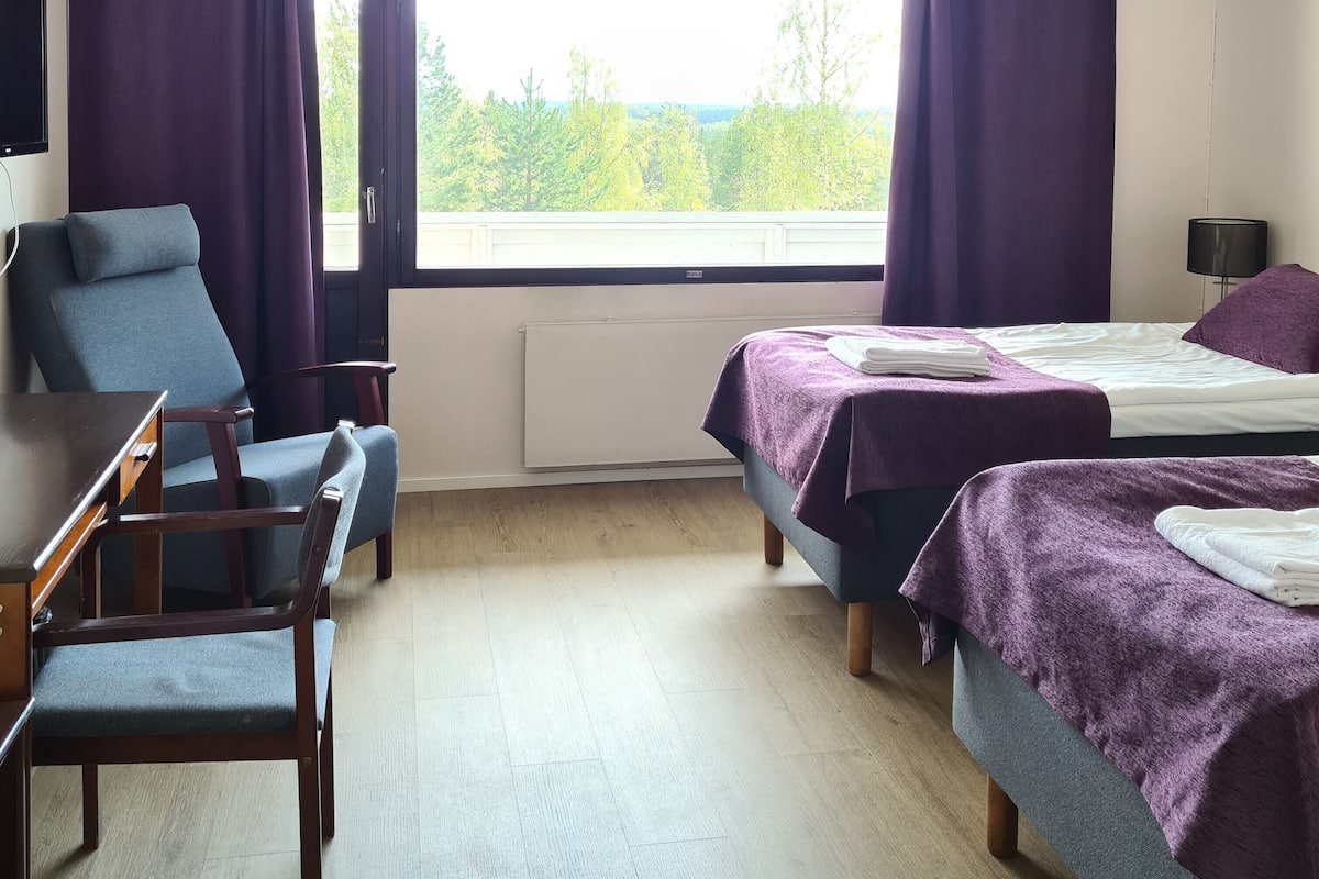 A hotel room with two beds, a desk, a chair, and a window with curtains.